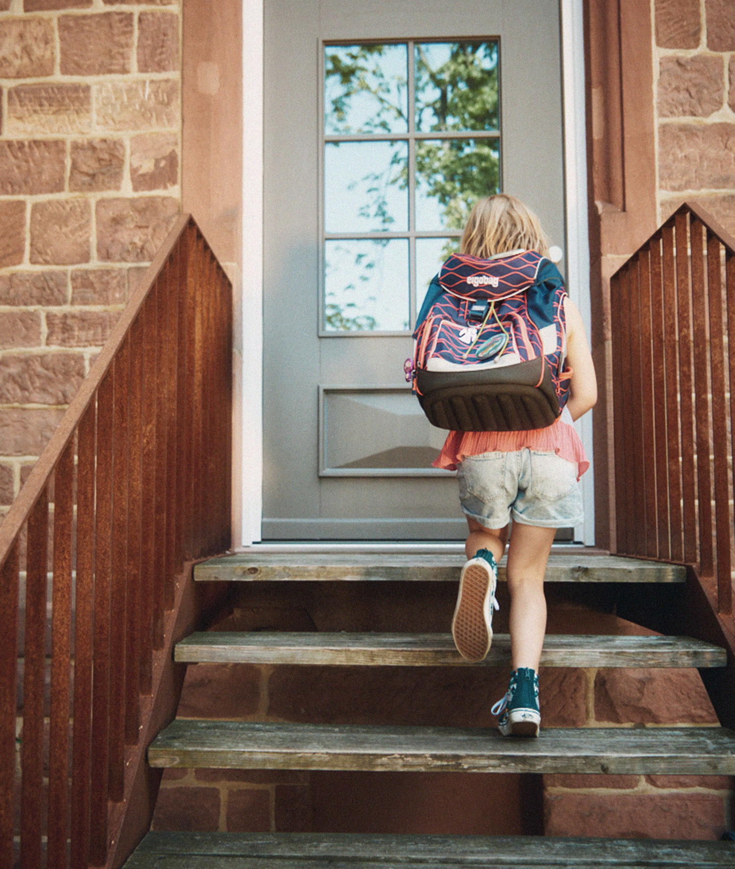Ein Kind mit Rucksack steigt die Treppen hoch, um ein Haus zu betreten.