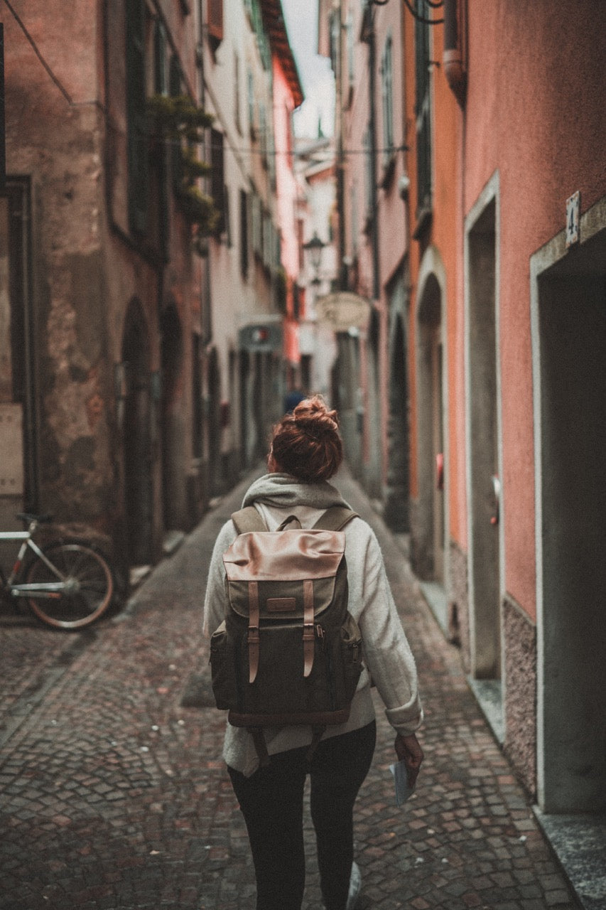 Eine Frau von hinten gesehen mit einem großen Rucksack, die durch eine authentisch wirkende, enge Straße geht.