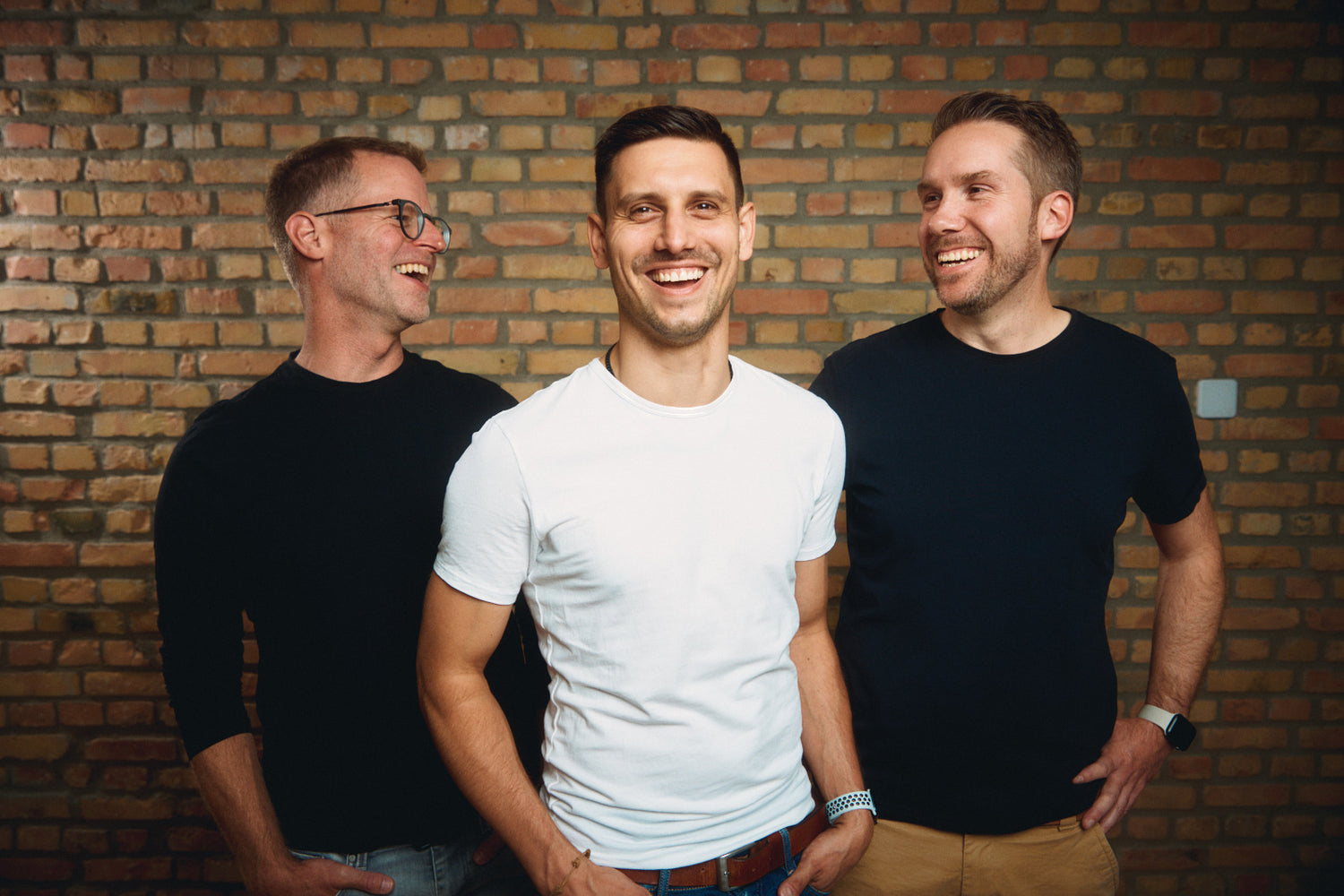 Drei Männer stehen vor einer Wand, lachen und posieren.
