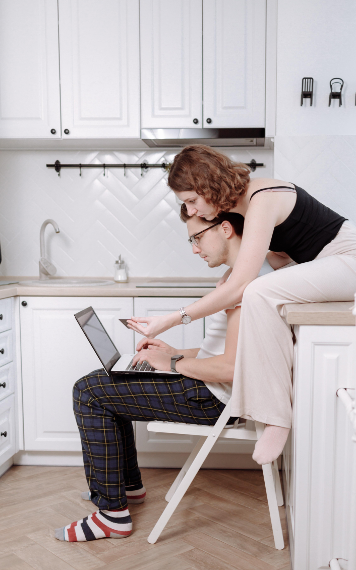 Ein Mann und eine Frau schauen sich in der Küche einen Laptop an.