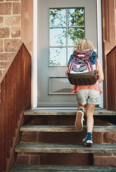 Ein Kind mit Rucksack steigt die Treppen hoch, um ein Haus zu betreten.